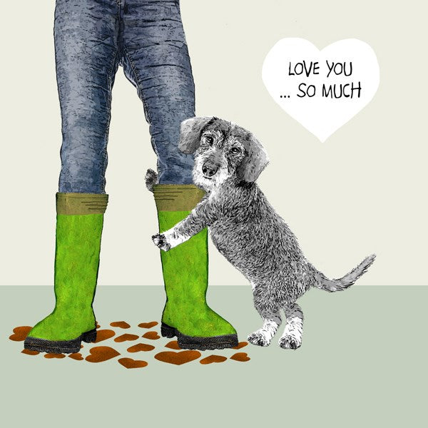 A dog hugging the legs of a person wearing welly boots and jeans with heart shaped muddy puddles.